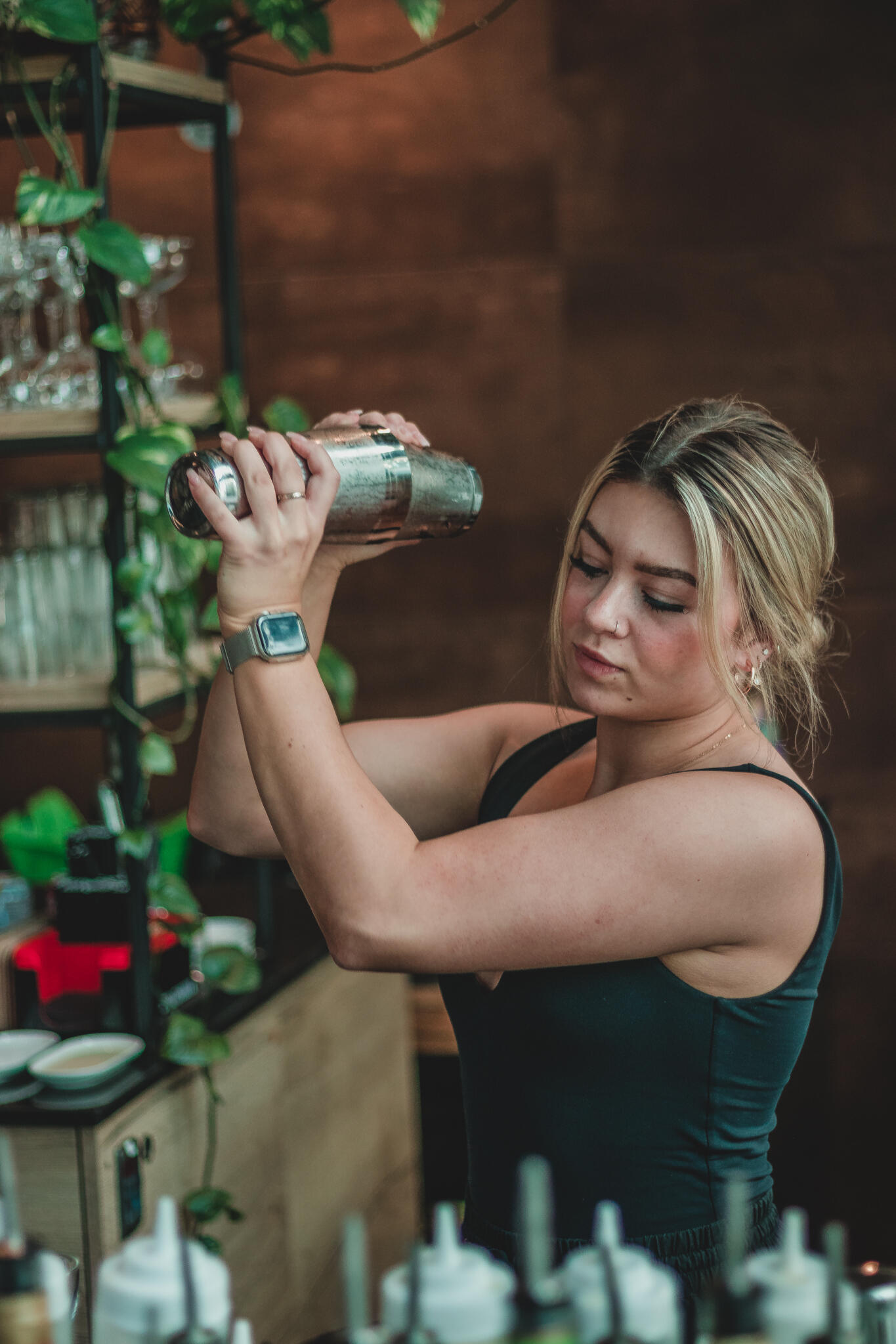 Gather Restaurant A woman mixes a cocktail at a bar, showcasing her bartending skills amidst an array of colorful liquor bottles.
