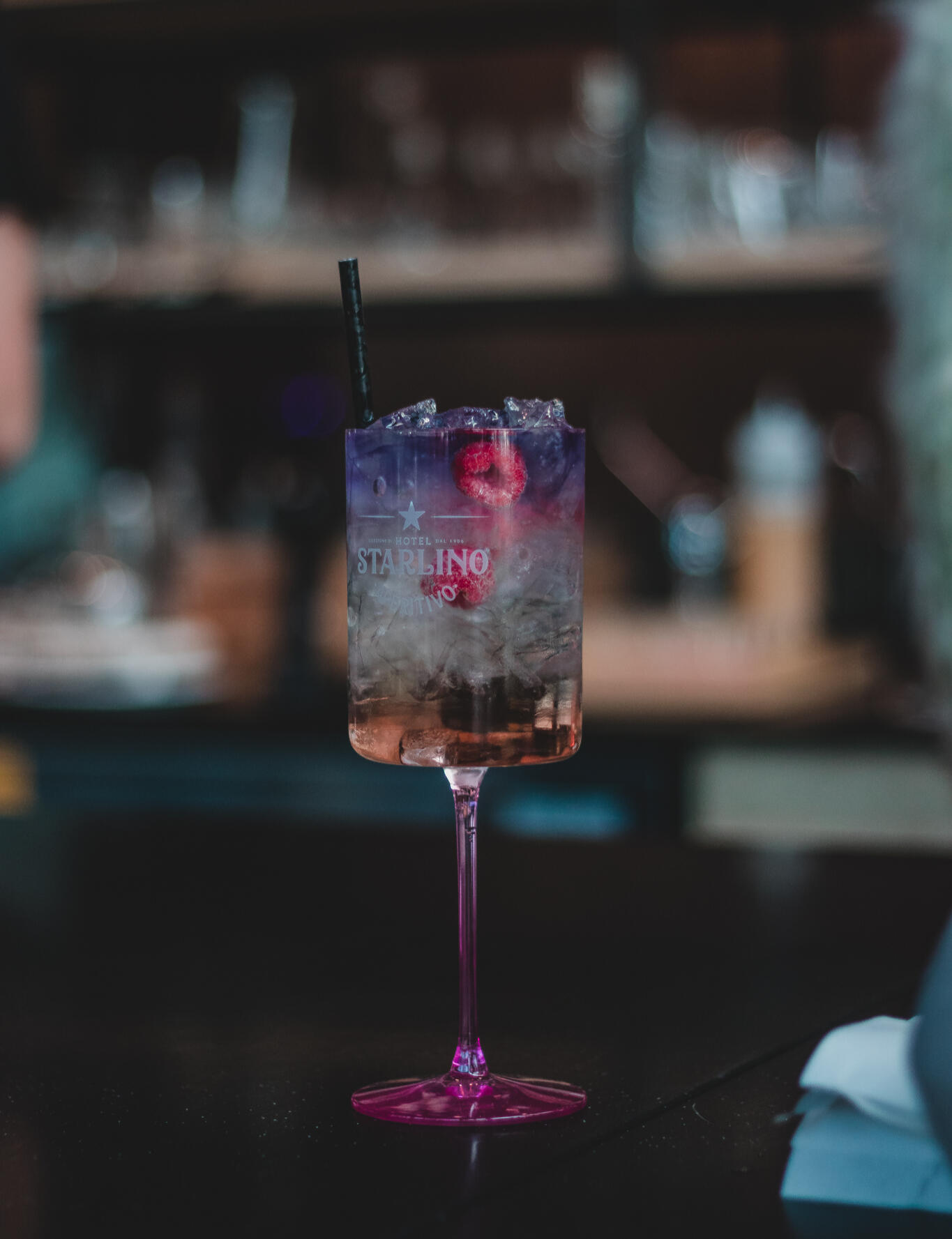 Gather Restaurant A vibrant purple cocktail drink in a pink glass, elegantly placed on a polished bar surface.