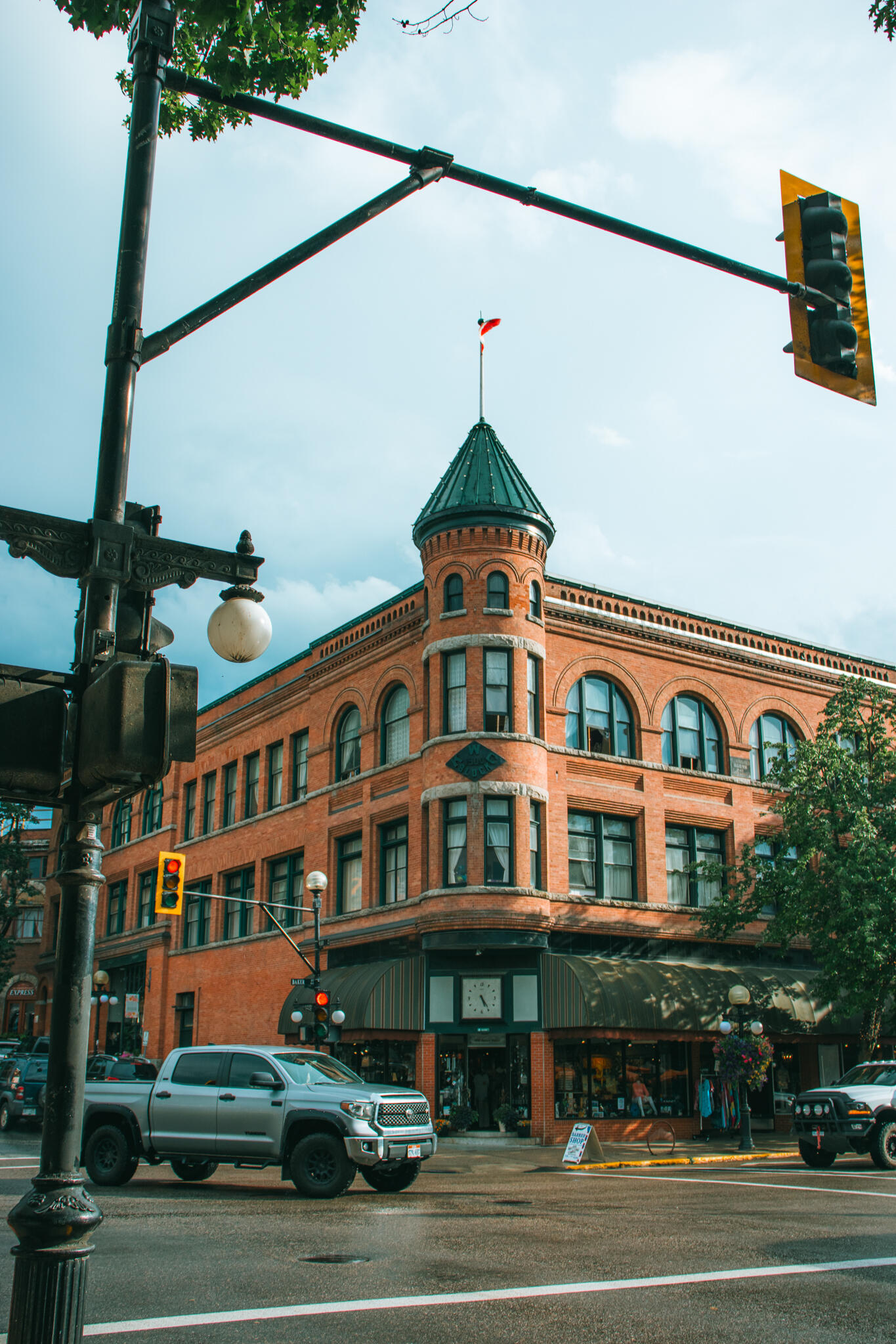 Nelson, British Columbia A towering old English Victorian style building with a distinctive clock tower, showcasing architectural details against a bright sky and a busy intersection of cars.