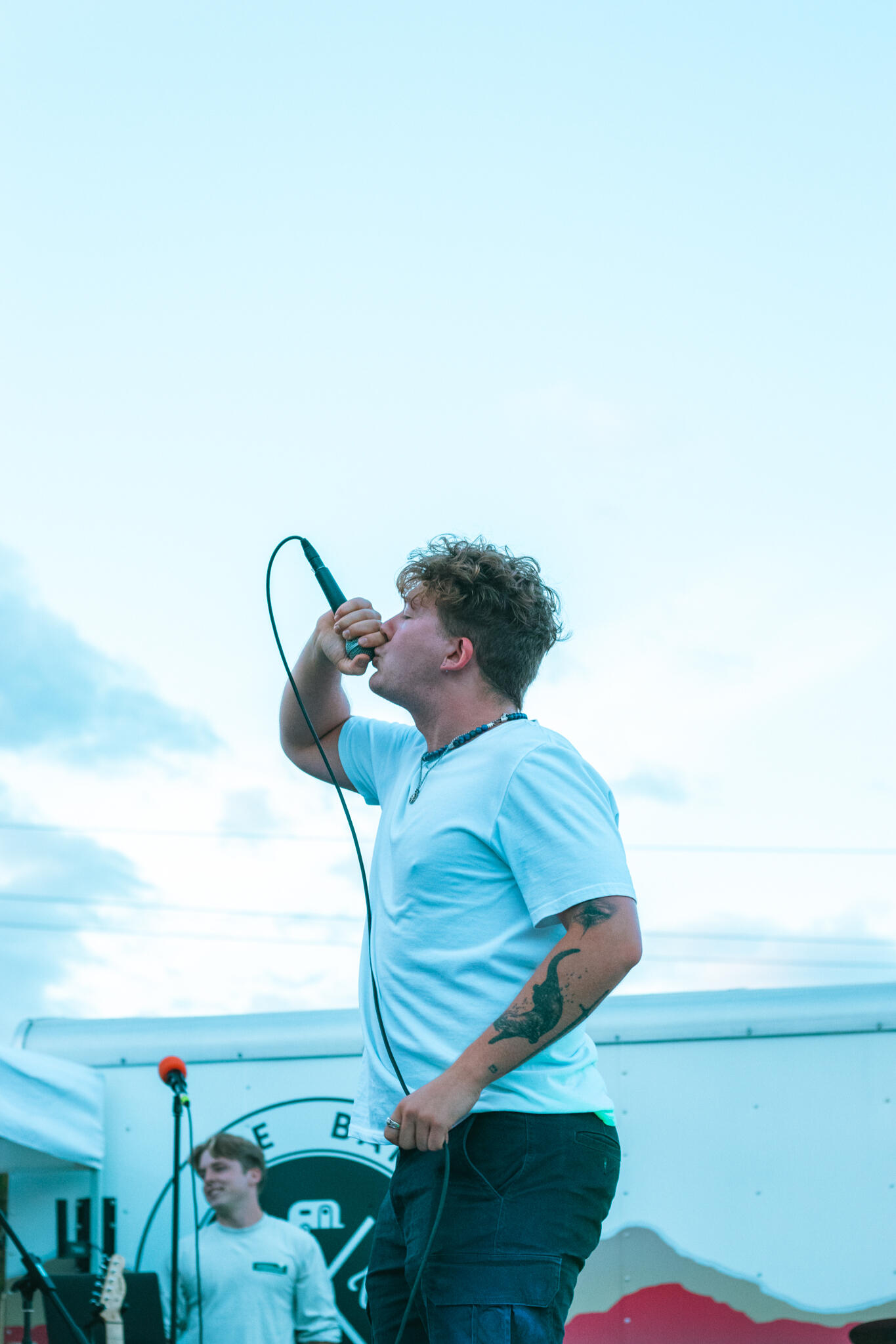 Never Ending Summer A man with tattoos on his arms sings into a microphone, expressing emotion through his performance.