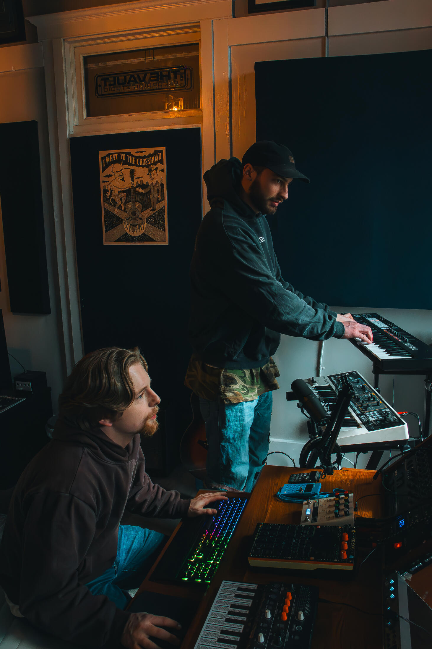 Vault 22 Multiple high-quality MIDI pianos and devices used to produce, mix, and master different music tracks, featured on a clean wood shelf with light shining on them.